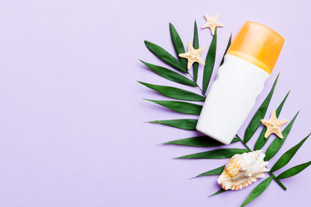 Sunscreen spray bottle. Bottle with sun protection cream and sea shells with tropical green leaf on color background, top view.の写真素材