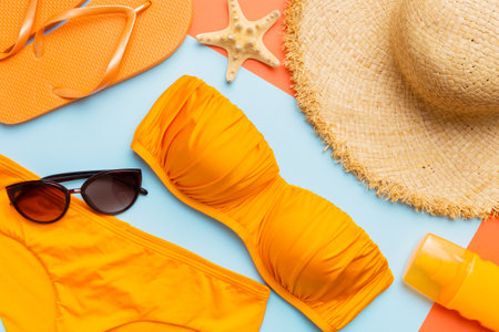 Woman swimwear and beach accessories flat lay top view on colored background Summer travel concept. bikini swimsuit, straw hat and seasheels. Copy space top view.の写真素材
