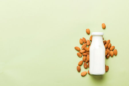 Top view of the almond milk in the glass bottle with almond nuts on the colored table. top view with copy space.の写真素材