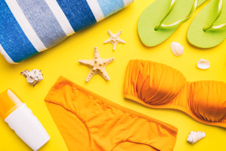 Woman swimwear and beach accessories flat lay top view on colored background Summer travel concept. bikini swimsuit, straw hat and seasheels. Copy space top view.の写真素材