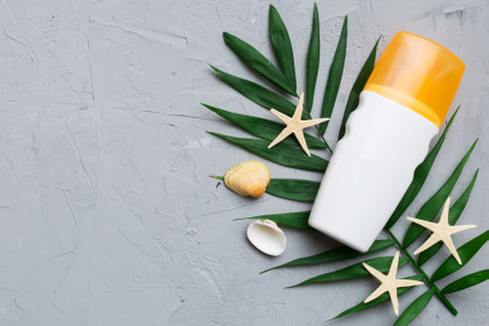 Sunscreen spray bottle. Bottle with sun protection cream and sea shells with tropical green leaf on...