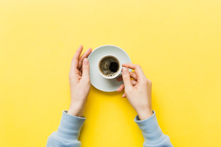 Minimalistic style woman hand holding a cup of coffee on Colored background. Flat lay, top view cappuccino cup. Empty place for text, copy space. coffee addiction. Top view, flat lay.の写真素材