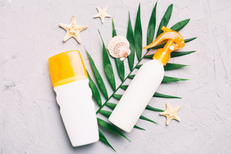 Sunscreen spray bottle. Bottle with sun protection cream and sea shells with tropical green leaf on...