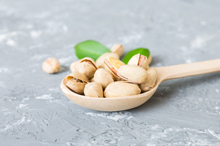 Close-up of tasty pistachio nuts in spoon with leaves on table background. top view. flat lay.