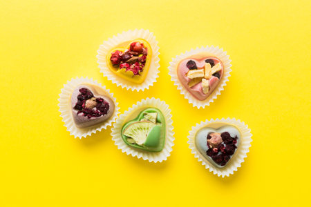 chocolate sweets in the form of a heart with fruits and nuts on a colored background. top view with...