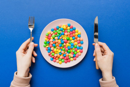the girl holds cutlery in her hands and eats sweets in a plate. Health and obesity concept, top view on colored background.の写真素材
