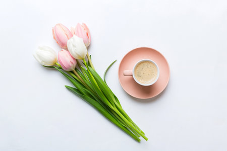 Spring background with flowers, a cup of coffee and a bouquet of pink and white tulips on colored table background with place for text. Copy space top view.の写真素材