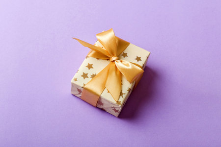 wrapped Christmas or other holiday handmade present in white paper with gold ribbon on colored...