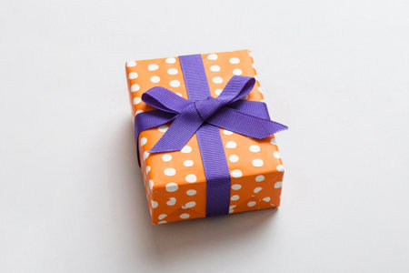 wrapped Christmas or other holiday handmade present in paper with purple ribbon on colored background. Present box, decoration of gift on colored table, top view with copy space.の写真素材