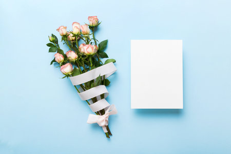 Greeting holiday card mockup with fresh roses on colored table background, mock up with copy space for design.の写真素材