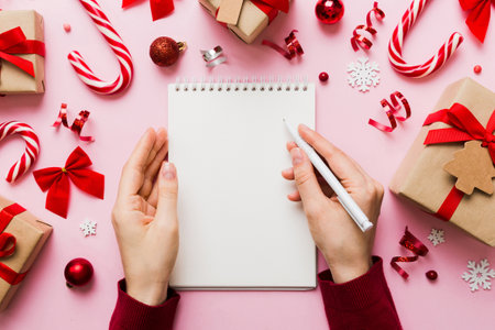 Woman writing Christmas to do list on notebook on colored background with xmas decorations.の写真素材