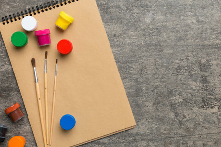 Album pages and paints, pencils, brushes on a colored background. Top view with empty space. workplace for creativity. home teaching concept drawing.の写真素材