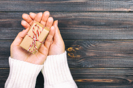 A woman hand holding christmas gift box on hand, on dark wooden background. top view with copy space. Toned.の写真素材