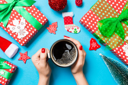 Top view of woman holding a cup of coffee in her hands on blue background. Christmas decorations. New year time concept.の写真素材
