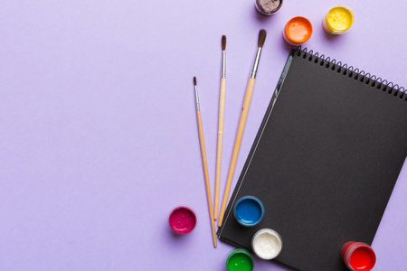 Album pages and paints, pencils, brushes on a colored background. Top view with empty space. workplace for creativity. home teaching concept drawing.の写真素材