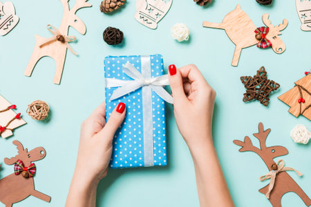 Top view of female hands holding a Christmas present on festive blue background. Holiday decorations and toys. New Year holiday concept.の写真素材