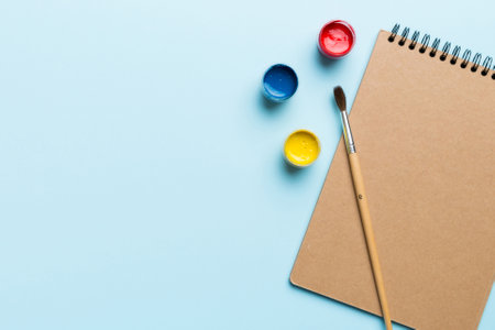 Album pages and paints, pencils, brushes on a colored background. Top view with empty space. workplace for creativity. home teaching concept drawing.の写真素材