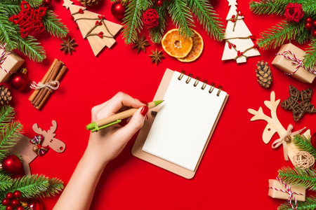 Top view of female hand making some notes in noteebok on colorful background. New Year decorations and toys. Christmas time concept.の写真素材