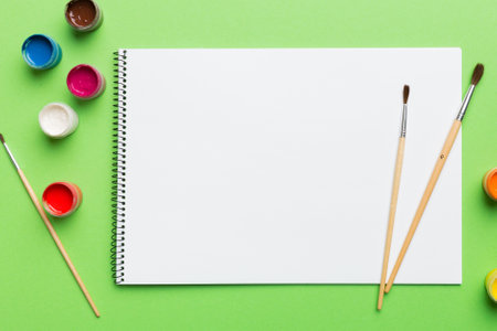 Album pages and paints, pencils, brushes on a colored background. Top view with empty space. workplace for creativity. home teaching concept drawing.の写真素材