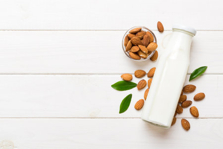 Top view of the almond milk in the glass bottle with almond nuts on the colored table. top view with copy space.の写真素材