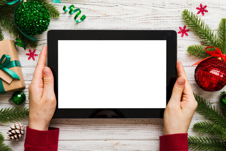 Christmas online shopping from home, female hands holding tablet pc with blank white display top view. woman hand holding tablet with blank screen, Christmas tree and gifts on background.の写真素材
