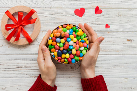 Female hands with delicious candies in box on color background.