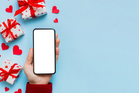 Woman hand holding mobile phone with blank screen on colored background with hearts, valentine day concept top view flat lay.の写真素材