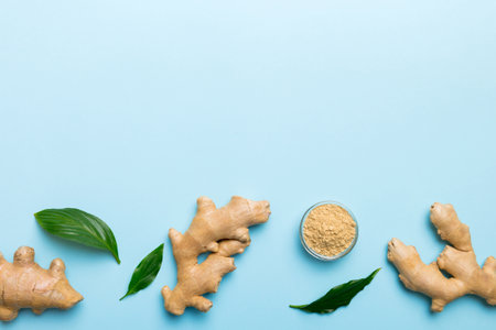 Finely dry Ginger powder in bowl with green leaves isolated on colored background. top view flat...
