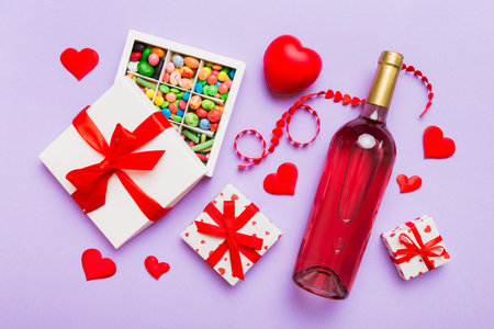 Bottle of red wine on colored background for Valentine Day with gift and chocolate. Heart shaped with gift box of chocolates top view with copy space.の写真素材
