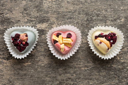 chocolate sweets in the form of a heart with fruits and nuts on a colored background. top view with...