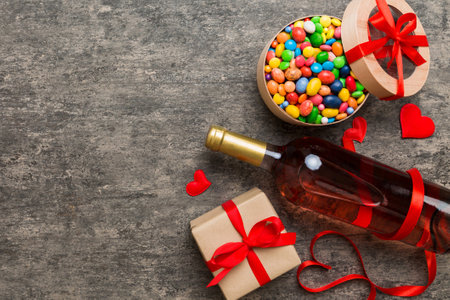 Bottle of red wine on colored background for Valentine Day with gift and chocolate. Heart shaped with gift box of chocolates top view with copy space.の写真素材