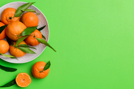 Fresh cutted clementines and whole mandarin over round plate on colored background. Food and drink...