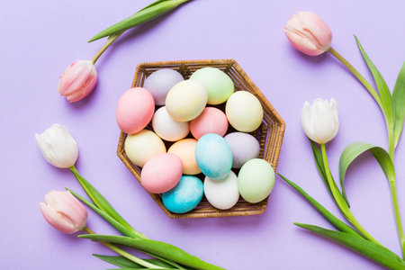 Happy Easter composition. Easter eggs in basket on colored table with yellow Tulips. Natural dyed colorful eggs background top view with copy space.の写真素材