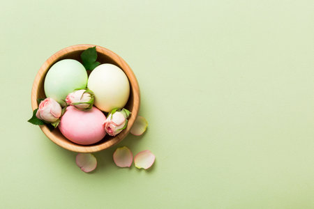 Happy Easter. Easter eggs in basket on colored table with yellow roses. Natural dyed colorful eggs background top view with copy space.の写真素材