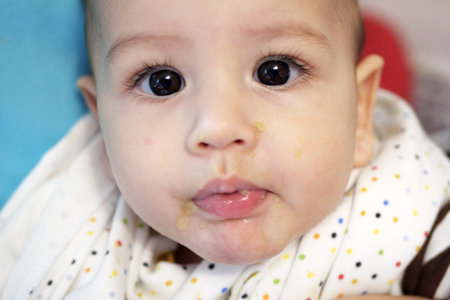 Portrait of little baby boy eating food. Baby with a spoon in feeding chair. Cute baby eating first...