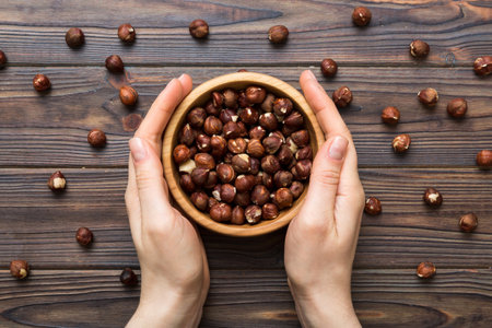 Woman hands holding a wooden bowl with hazelnut nuts. Healthy food and snack. Vegetarian snacks of different nuts.の写真素材