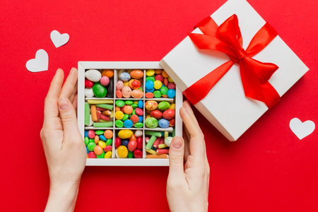 Female hands with delicious candies in box on color background.