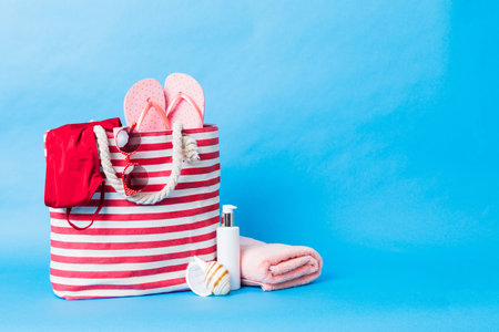 Stylish bag with beach accessories. Summer holiday concept. Top view of beach bag with sunscreen cream with space for text.の写真素材