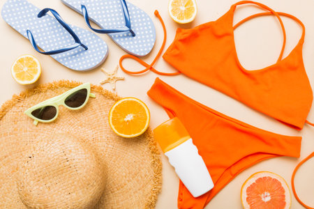 Swimming pool accessories concept. Top view of beach items on table, bright bikini, straw hat, and sunscreen skincare cream. Colorful beach wear. top view Flat lay, copy space.の写真素材