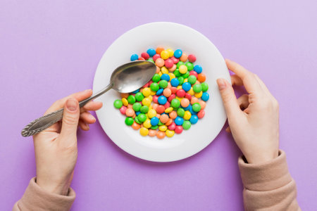 the girl holds cutlery in her hands and eats sweets in a plate. Health and obesity concept, top view on colored background.の写真素材