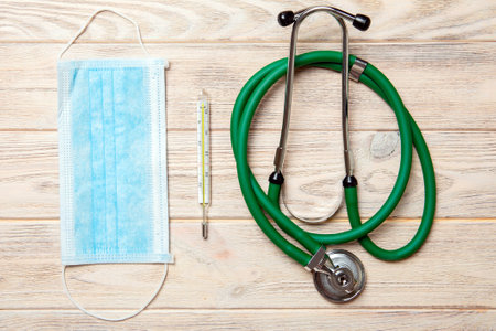 Top view of stethoscope, protective mask and thermometer on yellow wooden background. Medical instruments concept.の写真素材