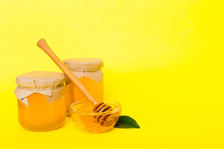 Honey in jar with leaves and honey dipper on colored background top view with copy text.の写真素材