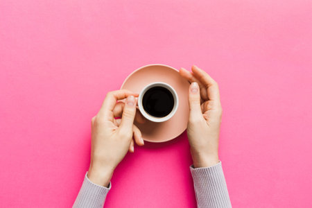 Minimalistic style woman hand holding a cup of coffee on colored background. Flat lay, top view cappuccino cup. Empty place for text, copy space. Top view, flat lay.の写真素材