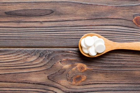 Heap of white pills on wooden background. Tablets scattered on a table. Pile of red soft gelatin capsule. Vitamins and dietary supplements concept.の写真素材