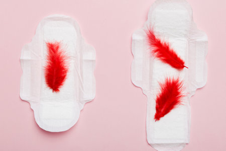 Women hygiene products or Sanitary pad with red feather on colored background. Pastel color. Closeup. Empty place for text. Female daily hygiene.の写真素材