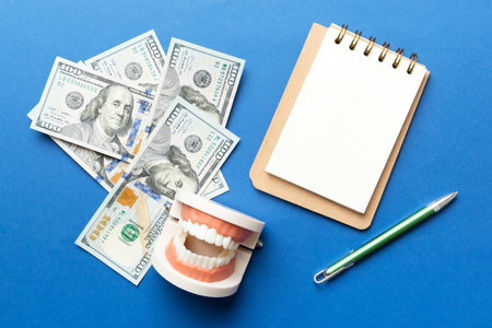 Flat lay composition with educational dental typodont model and money with notebook on colored...