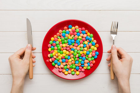 the girl holds cutlery in her hands and eats sweets in a plate. Top view on colored background.の写真素材