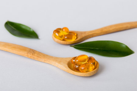 Vitamin omega capsules in a spoon on a colored background. Pills served as a healthy meal. Red soft gel vitamin supplement capsules on spoon.の写真素材