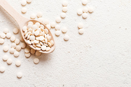 Heap of white pills on colored background. Tablets scattered on a table. Vitamins and dietary supplements concept.の写真素材