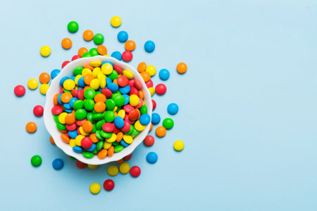Multicolored candies in a bowl on a colored background. birthday and holiday concept. Top view with copy space.の写真素材